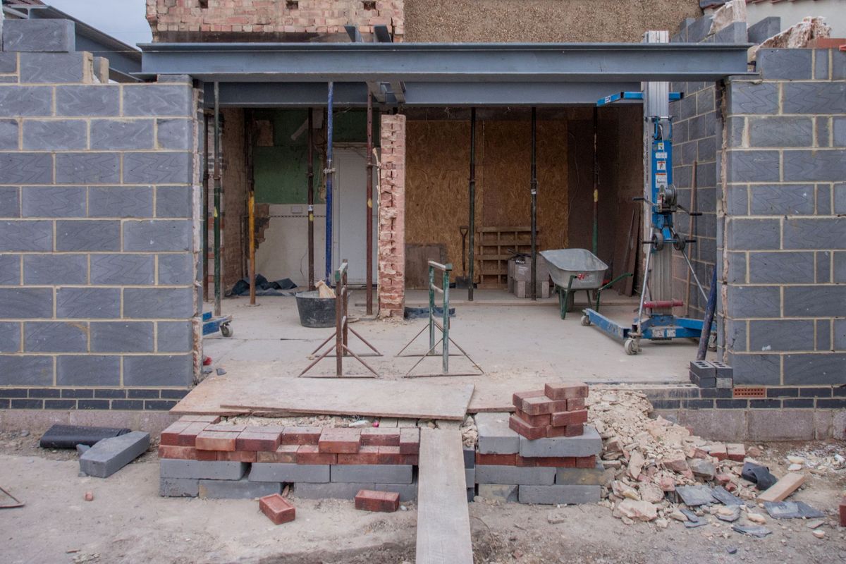 Een aanbouw achter een woning in opbouw, met nieuwe muren in blokken en een stalen balk.