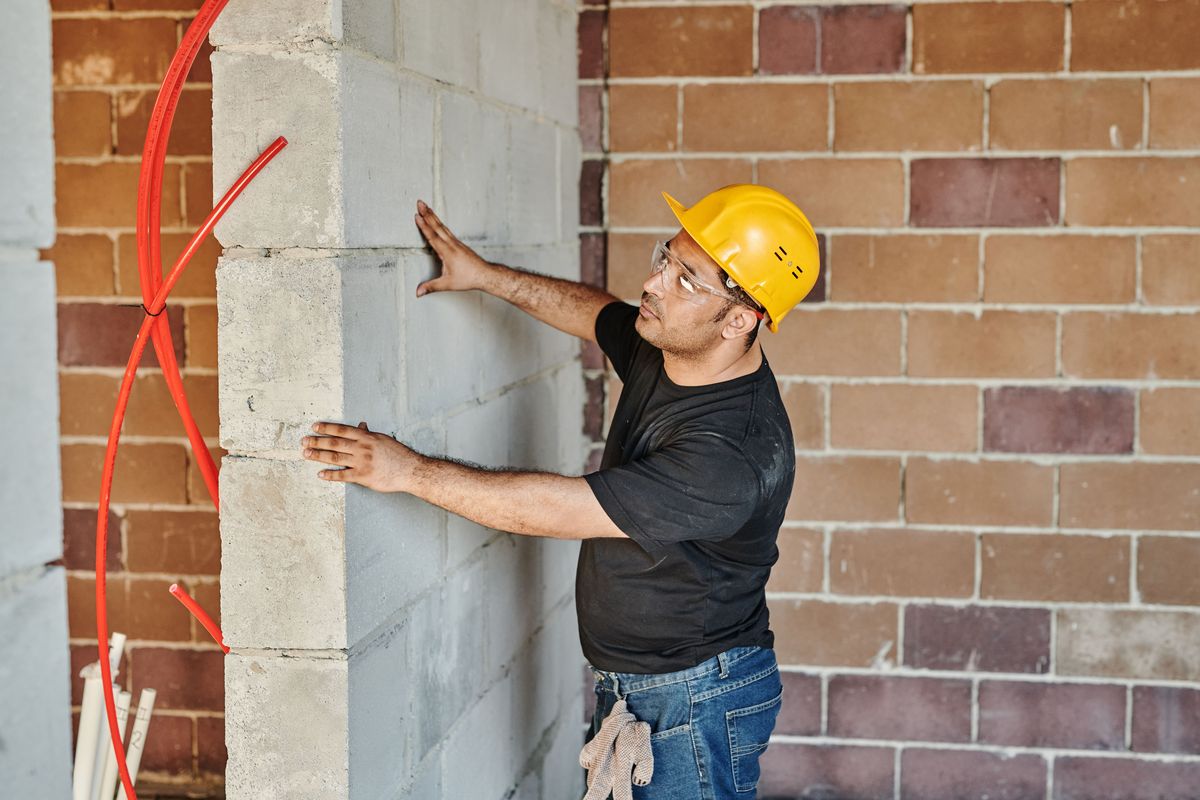 Een bouwvakker met gele helm controleert een binnenmuur in betonblokken.